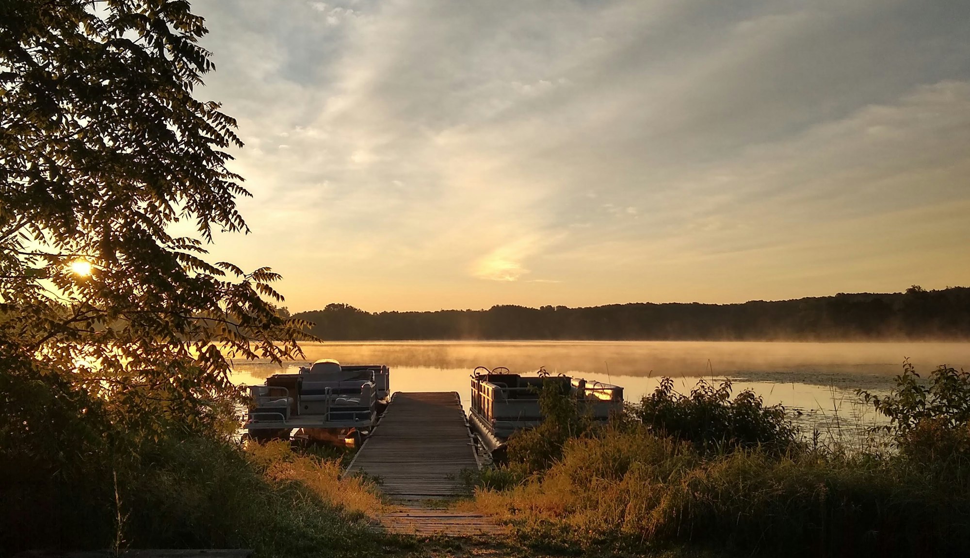 Two pontoon boats at a wooden dock on a misty Michigan lake at sunrise